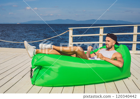 Young man enjoying leisure, lying on the air sofa Lamzac, near the sea 120340442