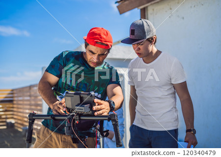 Steadicam operator and his assistant prepare camera and 3-axis stabilizer-gimbal for a commercial shoot Steadicam operator and his assistant prepare camera and 3-axis stabilizer-gimbal for a commercial shoot 120340479