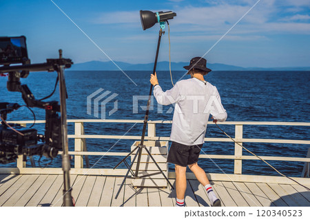 gaffer or the chief electrician in a motion-picture or television production unit set up the lights and light stand on a commercial shoot gaffer or the chief electrician in a motion-picture or television production unit set up the lights and light stand on a commercial shoot 120340523