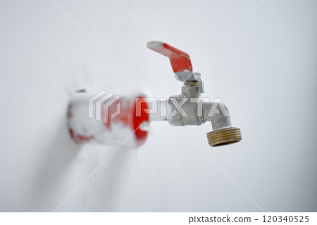 Close-up of water faucet with red handle protruding from white wall in empty apartment. Plumbing work during home renovation Close-up of water faucet with red handle protruding from white wall in empty apartment. Plumbing work during home renovation 120340525