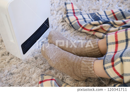 A woman warming her feet with a heater 120341711