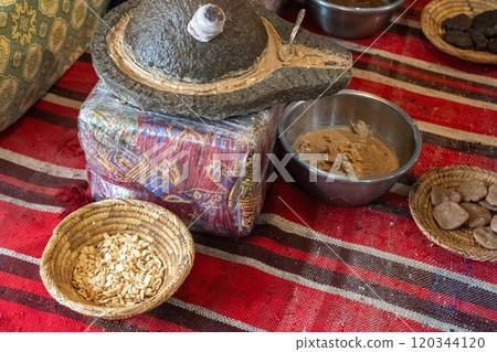 Traditional argan oil production setup, stone grinder, argan seeds, woven baskets, metal bowls, brown paste 120344120