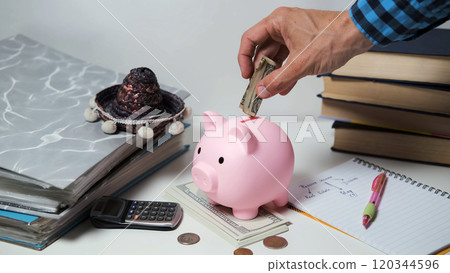 A man's hand placing money into a pink piggy bank on a table, symbolizing financial savings and investment 120344596
