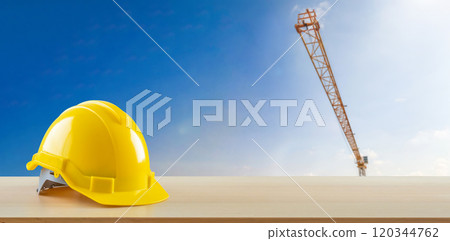 Yellow safety construction helmet on wood table with construction site background 120344762