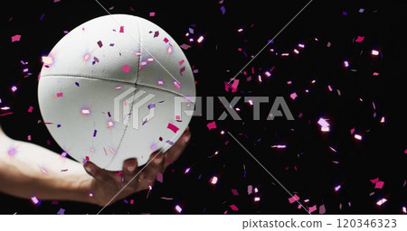Image of confetti over white rugby ball held by caucasian man's hand on black background 120346323