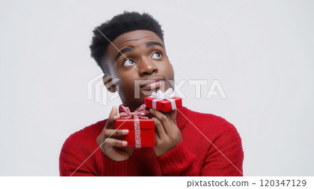Young man in red sweater holding gift boxes, contemplating holiday celebrations 120347129