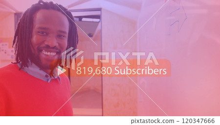 Smiling man in office with 829,020 subscribers image over him Smiling man in office with 829,020 subscribers image over him 120347666
