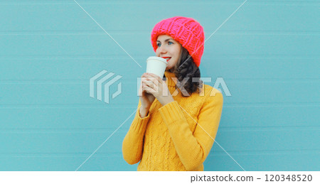 Happy smiling young woman with cup of coffee drink in winter hat, yellow sweater on blue background 120348520