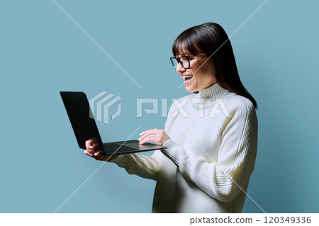 Smiling middle aged woman using laptop on blue background 120349336