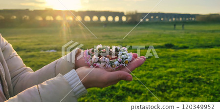 A delicate flower crown cradled in hands at sunset near an ancient aqueduct on a peaceful afternoon A delicate flower crown cradled in hands at sunset near an ancient aqueduct on a peaceful afternoon 120349952