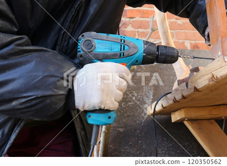 hands in gloves holding screwdriver wooden screwing a screw into a wooden productstructure, screwing long screw into structure of product, carpentry work on production of wood products with hand tool 120350562