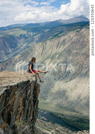 Dangerous photos in nature. A woman sits on the edge of a sheer cliff above a high cliff and dangles her legs 120350645