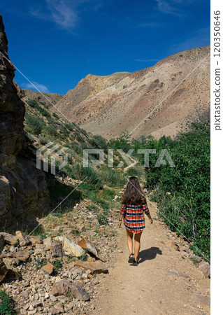 Woman with long hair in a red plaid shirt walks along a tourist trail in a canyon Kyzyl-Chin tract, Altai Mars 120350646