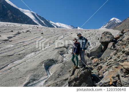 A couple of travelers, a woman and a man are standing near a glacier in the high mountains of Altai, Aktru 120350648