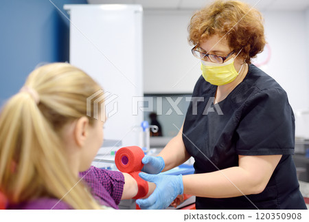 A phlebotomist nurse bandages the female patient's arm with a bandage after taking blood from a vein. A young woman performs laboratory tests during a medical examination. 120350908