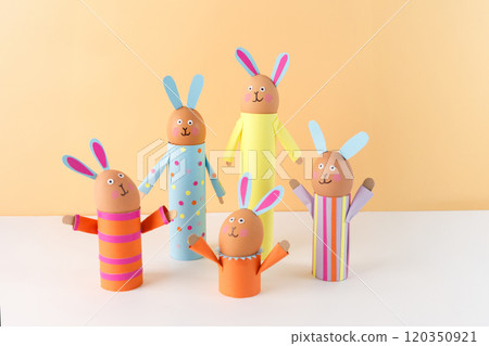 Handmade Easter bunny crafts using colored paper and eggs on a peach background. holder made of recycled toilet paper roll. Easter celebration and DIY craft concept. 120350921