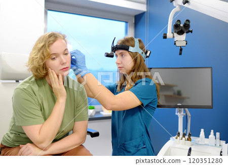 A patient is seen by an otolaryngologist. A professional ENT doctor examines a patient. An otolaryngologist examines a patient's inner ear using an otoscope 120351280