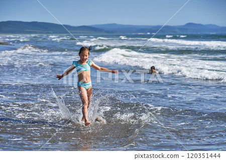 An 8 year old girl in a swimsuit having fun in the sea waves. An 8 year old girl in a swimsuit having fun in the sea waves. 120351444
