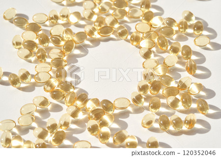 Scattered vitamin d soft gel capsules on white surface with natural sunlight 120352046