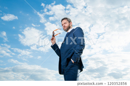 Businessman bottom view. Businessman in suit holding sunglasses. Grizzled businessman sky background Businessman bottom view. Businessman in suit holding sunglasses. Grizzled businessman sky background 120352856