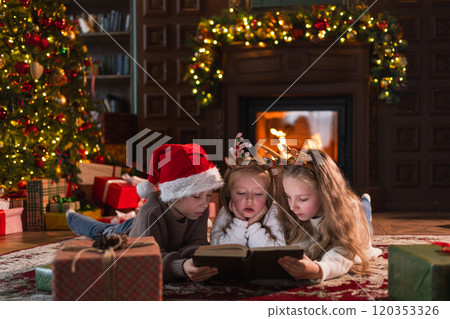 Merry Christmas Xmas holiday. Brother sisters children kids reading magic Christmas story book near Christmas tree in living room with fireplace in winter evening. Christmas eve at home Merry Christmas Xmas holiday. Brother sisters children kids reading magic Christmas story book near Christmas tree in living room with fireplace in winter evening. Christmas eve at home 120353326
