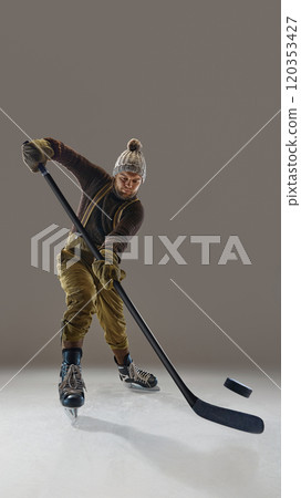 Man wearing pants with suspenders, knitted warm sweater and hat, in motion with stick, hitting puck. Winter sports and activity 120353427