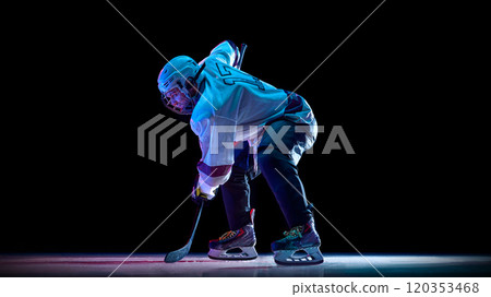 Man, professional hockey player dressed in white, standing into powerful skating stance on ice against black studio background in neon light 120353468