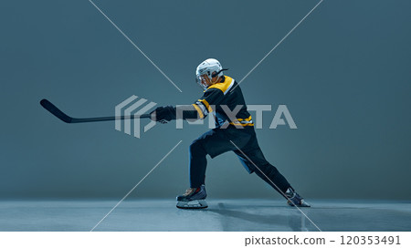 Man, professional ice hockey player dressed in black and yellow uniform, performing focused maneuver with stick and puck on ice rink 120353491
