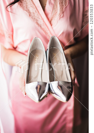Beautiful luxury bride in elegant white dress holds wedding shoes in the hands Beautiful luxury bride in elegant white dress holds wedding shoes in the hands 120353833