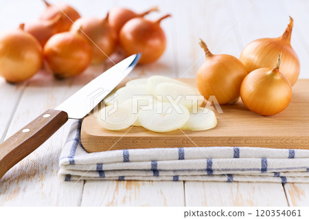 Sliced yellow onions in a cutting board on a light kitchen table. Sliced yellow onions in a cutting board on a light kitchen table. 120354061