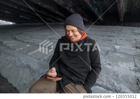 A person enjoying a moment of joy while sitting under a bridge, capturing memories on their smartphone during a cool day A person enjoying a moment of joy while sitting under a bridge, capturing memories on their smartphone during a cool day 120355012
