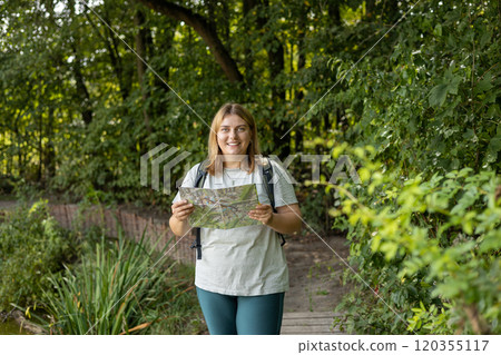 Stylish hipster woman holding paper map, wearing backpack and relaxing in nature. Travel and wanderlust concept. Amazing chill moment, summer time. Stylish hipster woman holding paper map, wearing backpack and relaxing in nature. Travel and wanderlust concept. Amazing chill moment, summer time. 120355117