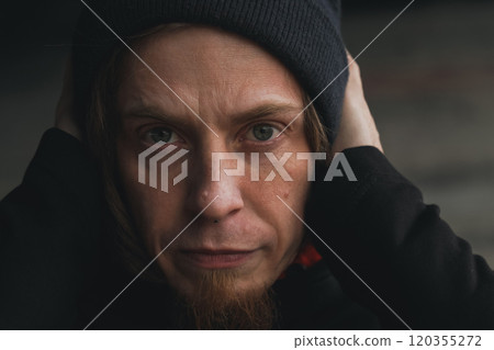 A contemplative youth with a beanie covers his ears in an urban setting, reflecting on life's challenges and emotions in the dim light A contemplative youth with a beanie covers his ears in an urban setting, reflecting on life's challenges and emotions in the dim light 120355272