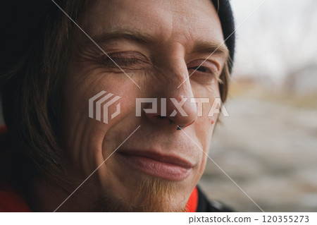 A man with a playful smile enjoying a moment outdoors during a chilly afternoon in a serene natural setting A man with a playful smile enjoying a moment outdoors during a chilly afternoon in a serene natural setting 120355273