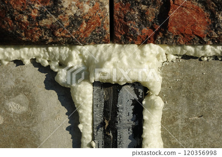 Construction foam is yellowish on a grayscale cement wall under red granite bricks 120356998