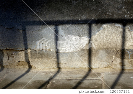 The shadow from the fence at the junction of the tiled sidewalk to the wall of the house foundation 120357131