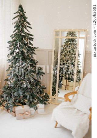 Bright living room with a cozy armchair and a large decorated Christmas tree 120362681