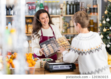 Female salesperson offers to buy cookies to teenage boy in Christmas interior of grocery supermarket 120363015