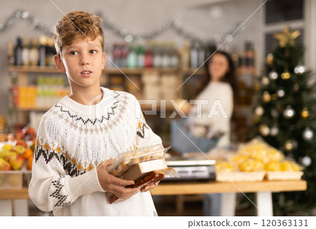 Teen boy selects sweets near window case in store, hold some package, New Year Eve Teen boy selects sweets near window case in store, hold some package, New Year Eve 120363131