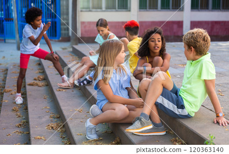 Positive tweenagers friendly blabbing while sitting on steps outdoors 120363140