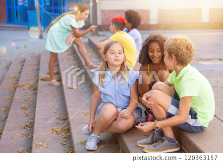 Happy tweenagers friends sitting on steps outdoors and chatting Happy tweenagers friends sitting on steps outdoors and chatting 120363157
