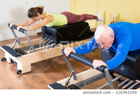 Elderly man performing pilates exercises on reformer during group workout Elderly man performing pilates exercises on reformer during group workout 120363209