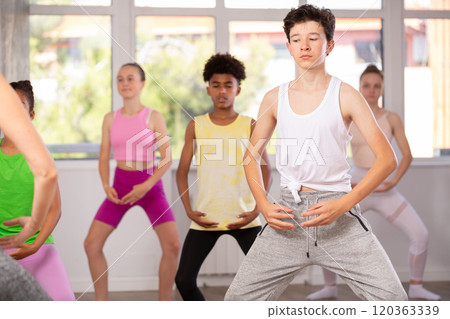 Thin teenage boy practicing plie position of ballet standing in row with others 120363339