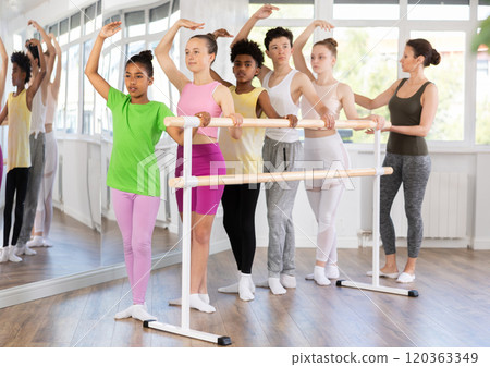 Black teen girl mastering third position at barre in ballet studio Black teen girl mastering third position at barre in ballet studio 120363349