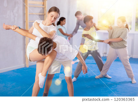 Tween girl applying armlock with elbow and knee blows to boy in mock bout at self-defense training Tween girl applying armlock with elbow and knee blows to boy in mock bout at self-defense training 120363365