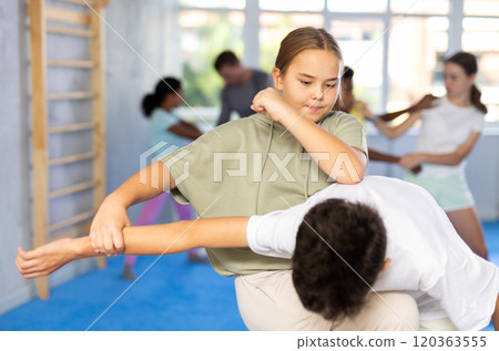 Girls and boys practicing in pair self defence movements with male trainer supervision 120363555