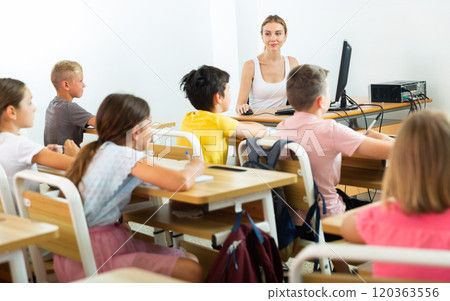 Female schoolteacher using computer during lesson with children 120363556
