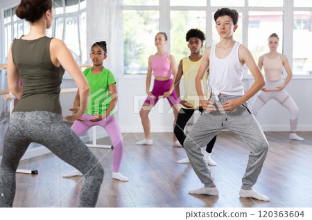 Thin teenage boy practicing plie position of ballet standing in row with others 120363604