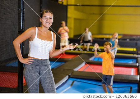 Happy young European female in white top and gray leggings posing on trampolines during active weekend free time in entertainment center 120363660