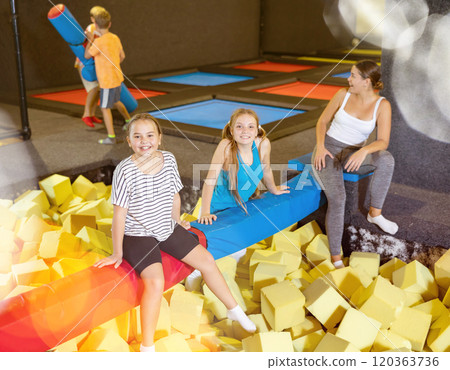 Company of joyful smiling children sitting together on crossbar in entertainment trampoline centre surrounded with foam cubes Company of joyful smiling children sitting together on crossbar in entertainment trampoline centre surrounded with foam cubes 120363736